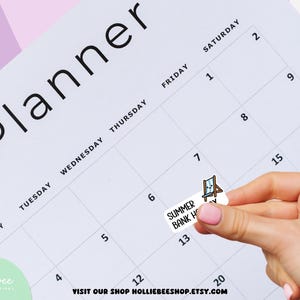 May include: A white rectangular planner sticker featuring the text SUMMER BANK HOLIDAY and a small illustration of a blue and white striped beach chair. The sticker is being placed onto a grid-style weekly planner page with black text.