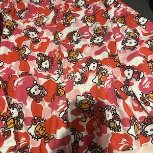 May include: A pink, red, and white patterned button-up shirt. The pattern features a camouflage design with cartoon characters. The shirt has a pocket on the front and a collar.
