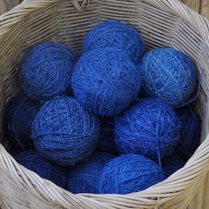 May include: A wicker basket filled with balls of blue yarn. The basket is hanging from a bamboo fence.