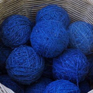 May include: A wicker basket filled with balls of blue yarn. The yarn is tightly wound and has a rough texture.