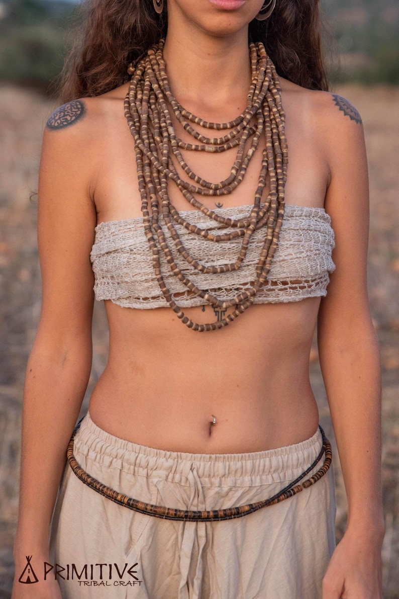 May include: A woman wearing a beige top and pants with a brown beaded necklace and a brown beaded belt.