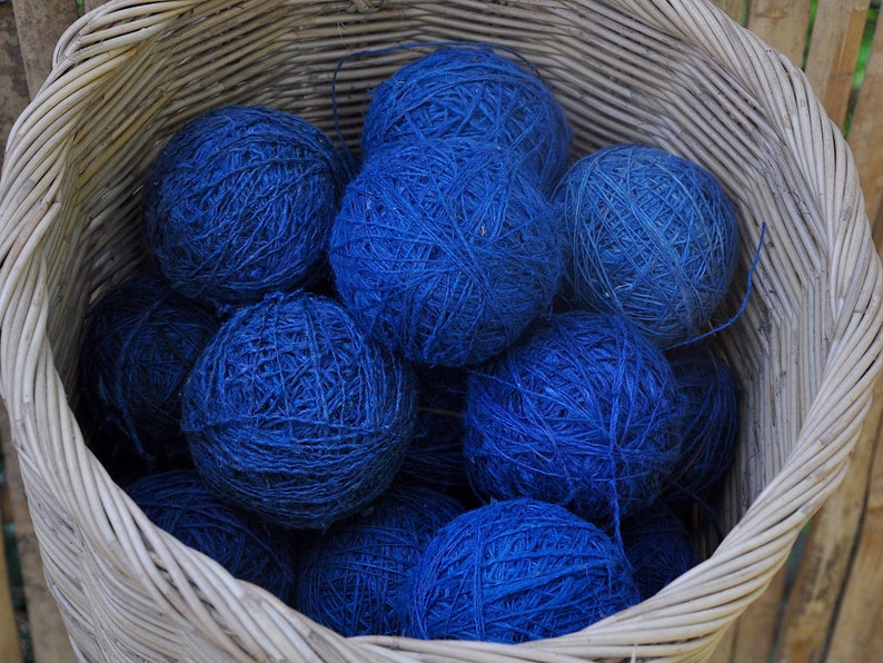 May include: A wicker basket filled with balls of blue yarn. The yarn is tightly wound and has a rough texture.