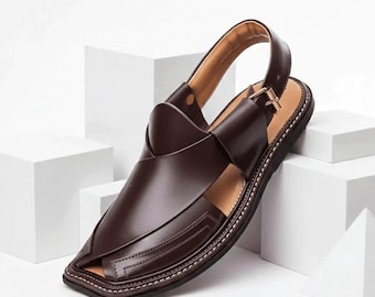 May include: A dark brown leather sandal featuring a closed-toe design with overlapping straps, a slingback strap with a metal buckle, and a flat sole with visible white stitching along the edge of the footbed.