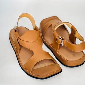 May include: A pair of tan leather sandals with square toes and adjustable ankle straps. The sandals have a stitched sole and a simple, open design, suitable for casual wear.