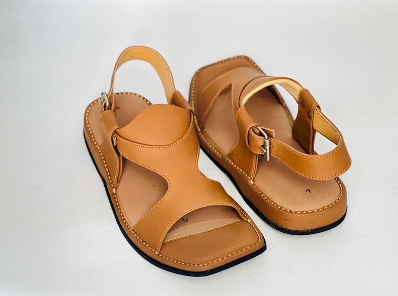 May include: A pair of tan leather sandals with square toes and adjustable ankle straps. The sandals have a stitched sole and a simple, open design, suitable for casual wear.