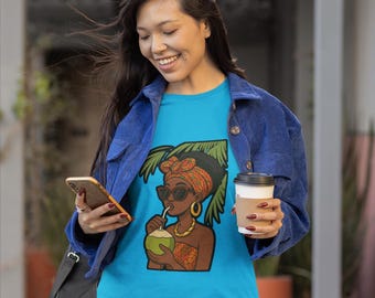 Puede incluir: Una camiseta azul claro con un gráfico de una mujer bebiendo de un coco, con gafas de sol y un pañuelo en la cabeza. La mujer lleva joyas de oro. La persona lleva una chaqueta de pana azul y pantalones cortos vaqueros.