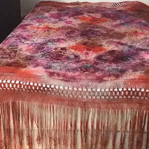 May include: A colorful, fringed shawl with a floral pattern. The shawl features a blend of pink, purple, and orange hues, with a detailed fringe along the bottom edge. The intricate design and warm colors create a cozy and artistic aesthetic.