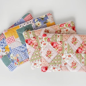 May include: Four quilted zipper pouches in various floral and patchwork patterns. The pouches feature a mix of colors, including pink, blue, yellow, and green. The designs include floral prints, gingham, and striped fabrics.