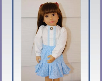 May include: A PDF pattern for a pleated skirt and blouse for a doll. The doll is wearing a white blouse with blue trim and a blue and white patterned skirt. The doll has brown hair and brown eyes. The pattern is available from Wind Woman Designs.