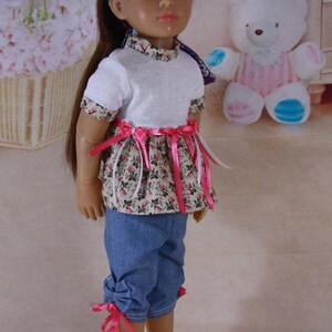 May include: A doll with long brown hair wearing a white t-shirt with a pink and white floral print skirt, a pink ribbon tied around the waist, and blue denim pants with pink ribbon ties at the bottom.