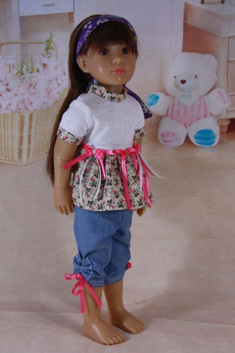 May include: A doll with long brown hair wearing a white t-shirt with a pink and white floral print skirt, a pink ribbon tied around the waist, and blue denim pants with pink ribbon ties at the bottom.