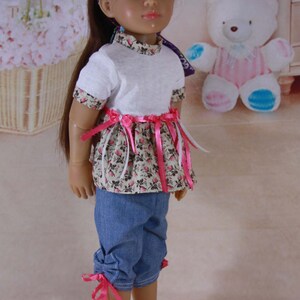 May include: A doll with long brown hair wearing a white t-shirt with a floral print skirt and denim pants with pink ribbon ties. The doll is wearing a purple headband with a peace sign design.
