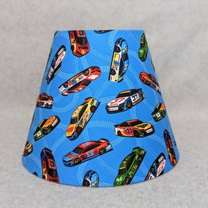 May include: A blue lampshade with a pattern of colorful race cars on a blue background. The cars are all different colors and have different numbers on them.