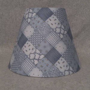 May include: A gray and white lampshade with a patchwork design. The lampshade is made of fabric and has a conical shape.