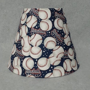 May include: A blue lampshade with a baseball pattern. The lampshade is covered in white baseballs with red stitching and the word "Baseball" repeated throughout the design. The background is a dark blue with white stars.