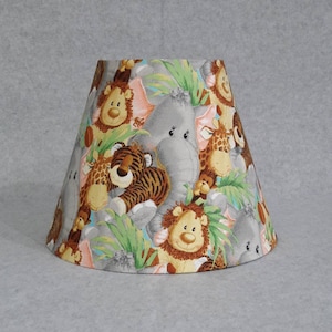 May include: A lampshade with a colorful print of cartoon animals, including a lion, elephant, tiger, and giraffe. The animals are surrounded by green leaves and flowers.