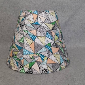 May include: A white lampshade with a geometric pattern in shades of green, blue, pink, and black.