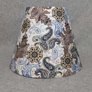 May include: A white lampshade with a paisley pattern in shades of blue, brown, and green.
