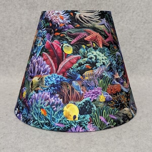 May include: A lampshade with a colorful underwater scene featuring coral reefs, fish, and starfish. The fabric is a dark blue with vibrant colors of pink, purple, yellow, and orange.
