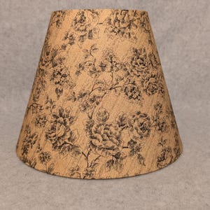 May include: A beige lampshade with a black floral pattern. The lampshade is made of fabric and has a conical shape.