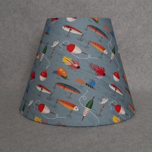May include: A blue lampshade with a pattern of fishing lures, including red and white bobbers, green and white lures, and yellow and orange lures.