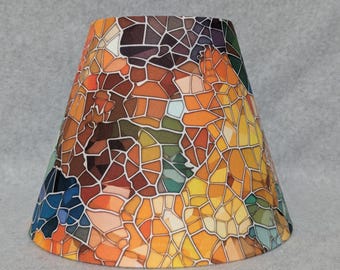 May include: A tapered drum lampshade featuring a multi-colored mosaic pattern. The design consists of irregular geometric shapes in shades of orange, yellow, brown, blue, and green, separated by thin white lines, creating a stained glass effect.