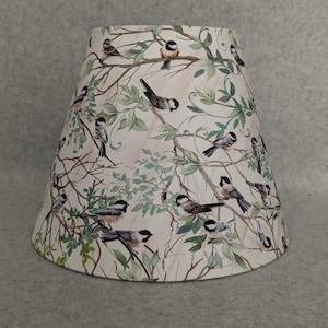 May include: A white lampshade with a pattern of birds and leaves. The birds are black and white and the leaves are green.
