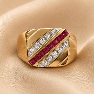 May include: A gold ring featuring a central diagonal channel of square-cut red rubies flanked by two parallel rows of round-cut white diamonds. The polished gold band has a wide, tapered design with subtle grooved detailing on the sides.