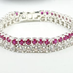 May include: A silver bracelet with two rows of gemstones. The top row features vibrant red gemstones, while the bottom row showcases clear, square-cut stones. The bracelet is designed with a secure clasp.