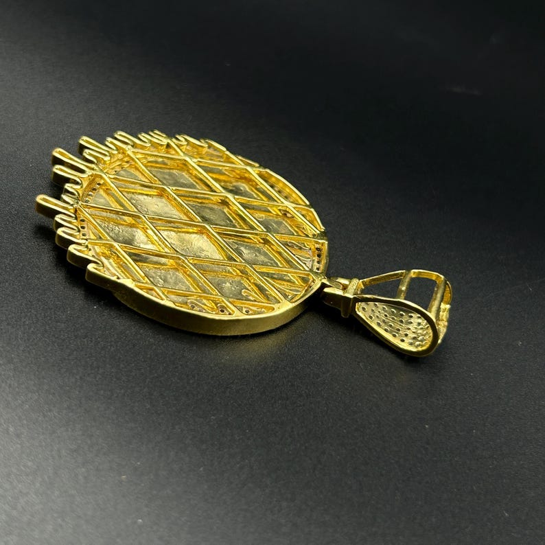 Op de afbeelding: Een goudkleurige hanger met een ruitvormig patroon. De hanger heeft een getextureerd oppervlak en een beugel om aan een ketting te bevestigen. De hanger is waarschijnlijk gemaakt van verguld metaal.