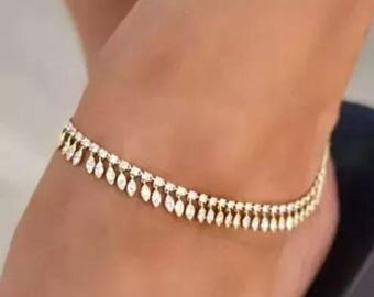 May include: A gold-colored anklet with dangling teardrop-shaped embellishments. The anklet is worn on a person's ankle, showcasing the delicate design and sparkling details. The jewelry piece is a stylish accessory.