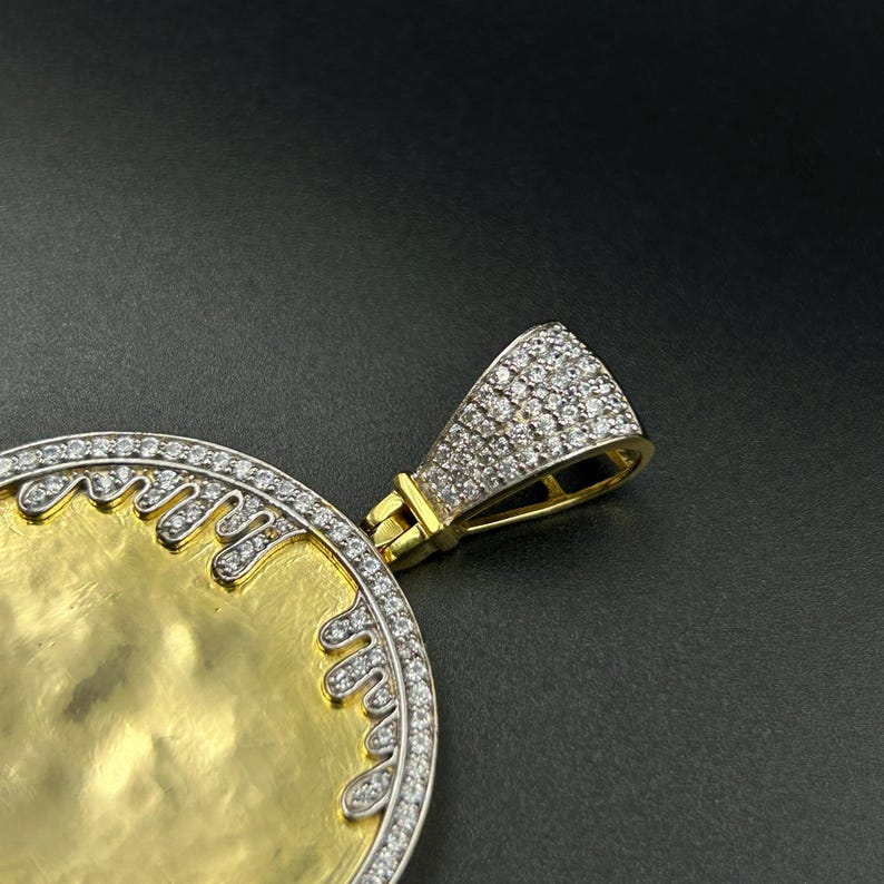 Op de afbeelding: Een gouden hanger met een cirkelvormig ontwerp en een met diamanten bezette beugel. De hanger heeft een gouden midden met een decoratieve rand van kleine diamanten. De beugel is ook bedekt met kleine diamanten.