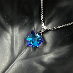 May include: A silver necklace featuring a large, faceted pendant with a vibrant blue and purple color gradient. The pendant is a geometric shape, reflecting light. The chain is a delicate, linked design, creating a striking contrast with the pendant.