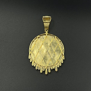 Op de afbeelding: Een goudkleurige hanger met een ruitvormig midden en een decoratieve, druipende rand. De hanger heeft een beugel voor een ketting en staat tegen een donkere achtergrond. Het sieraad is waarschijnlijk gemaakt van metaal en heeft een gedetailleerd ontwerp.