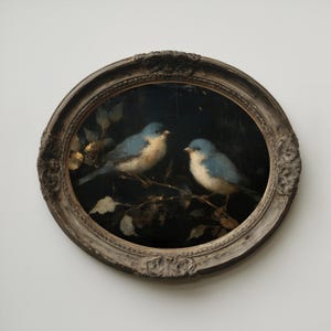 May include: Oval framed painting featuring two bluebirds perched on a branch with leaves. The birds have blue feathers and white bellies. The frame is ornate with a distressed, antique finish. The background is dark.
