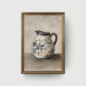 Könnte beinhalten: Gerahmtes Kunstwerk mit einer weißen Kanne mit blauen Blumenmustern und einem dunkelblauen Rand. Die Kanne hat einen Henkel und einen Ausguss. Das Kunstwerk ist vor einem neutralen Hintergrund platziert und in einem goldfarbenen Rahmen gerahmt.