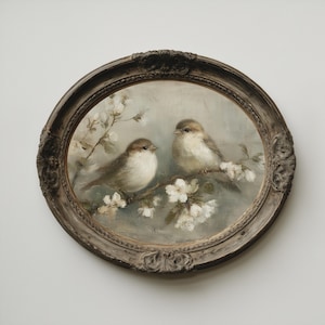 Puede incluir: Pintura ovalada que representa dos pequeños pájaros posados en una rama florecida. Los pájaros tienen plumas marrones y blancas, y las flores son blancas. La pintura está enmarcada en un marco decorativo y ornamentado de tonos oscuros.