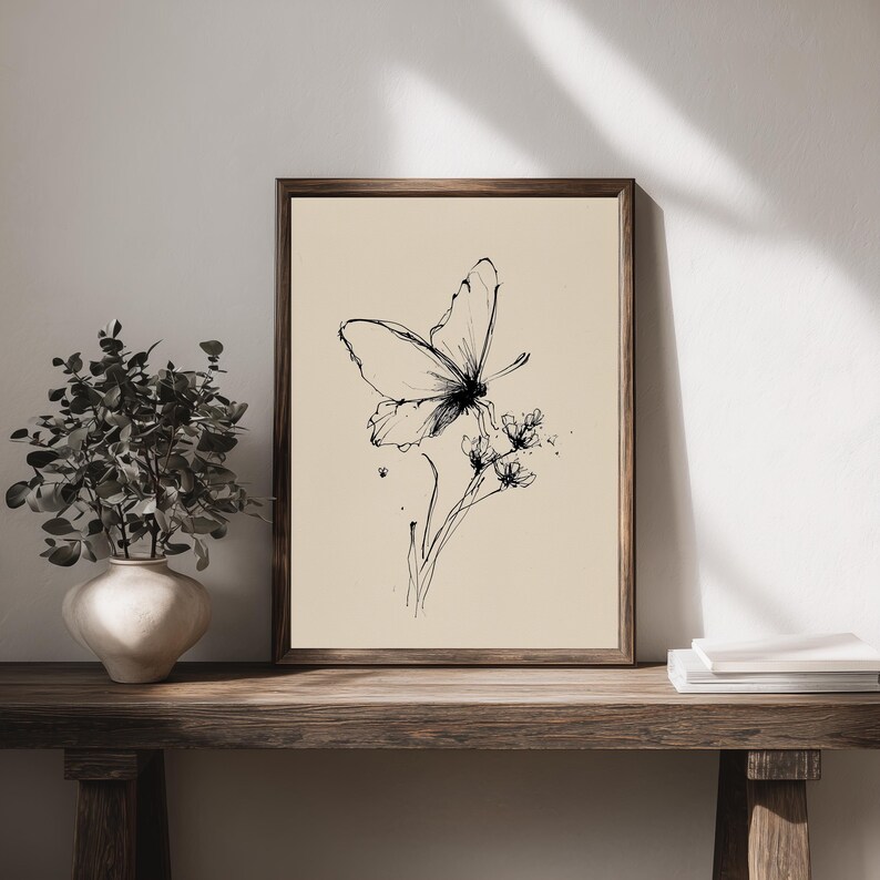 May include: A framed art print featuring a black and white butterfly illustration. The butterfly is perched on delicate flowers, rendered in fine lines against a cream-colored background. The artwork is displayed in a dark wooden frame, adding a touch of rustic charm.