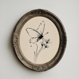 May include: Oval framed artwork featuring a black ink drawing of a butterfly perched on a flower. The butterfly and flower are centered on a cream-colored background. The frame is a distressed, ornate, dark brown color.