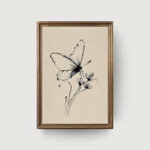 May include: A framed black and white ink drawing of a butterfly perched on delicate flowers. The artwork features fine lines and shading, set against a neutral background. The frame is a warm gold color, adding a touch of elegance to the botanical illustration.