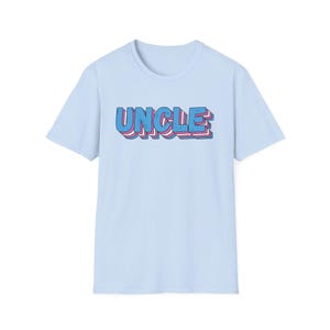 May include: Pale blue t-shirt featuring the word "UNCLE" in a 3D design, using blue and pink colours. The shirt has a crew neck and short sleeves. The text is positioned centrally on the front.