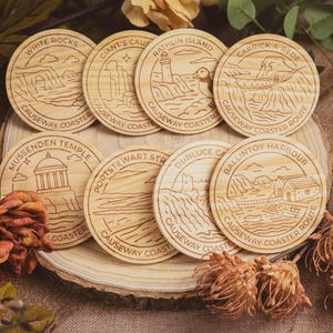 May include: Eight circular wooden coasters, each engraved with a different Northern Irish landmark and the words "Causeway Coaster". The designs include "White Rocks", "Giant's Caus", and "Carrick-a-Rede", offering a rustic, natural aesthetic.