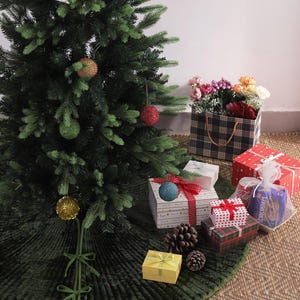 Puede incluir: Un &aacute;rbol de Navidad decorado con adornos y una falda de &aacute;rbol verde. Varios regalos envueltos en varios patrones y colores est&aacute;n dispuestos alrededor de la base del &aacute;rbol, junto con pi&ntilde;as y una caja de flores.