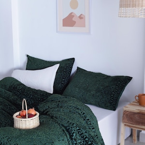 Può includere: Un letto con biancheria da letto verde scuro con un motivo. Ci sono due cuscini abbinati e un cuscino bianco. Un piccolo cestino di frutta è appoggiato sul letto. Un'immagine incorniciata è appesa al muro.