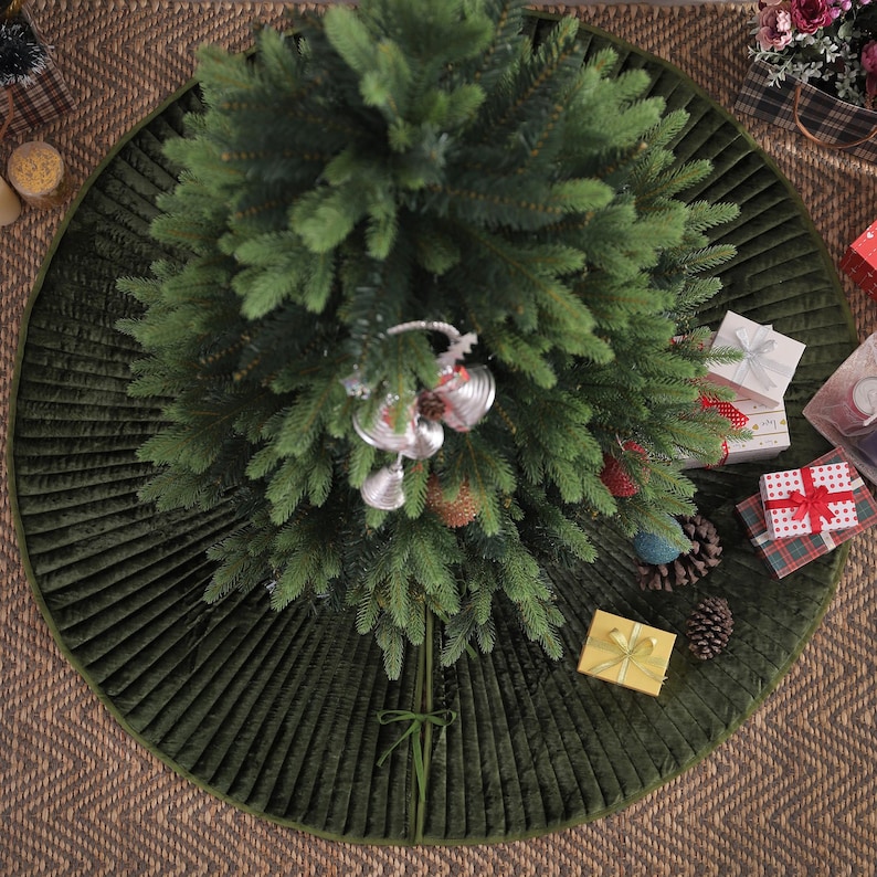 Puede incluir: Vista a&eacute;rea de un &aacute;rbol de Navidad decorado con una falda de &aacute;rbol acolchada verde. Campanas y adornos plateados cuelgan del &aacute;rbol. Varios regalos envueltos y pi&ntilde;as est&aacute;n esparcidos alrededor de la base del &aacute;rbol.