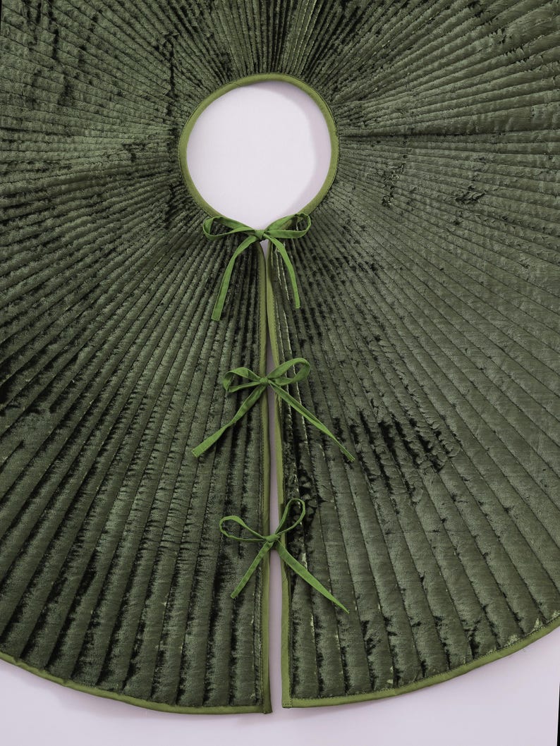 Puede incluir: Una falda de &aacute;rbol de Navidad de terciopelo verde con una abertura circular y un dise&ntilde;o plisado radiante. La falda tiene un ribete verde y se asegura con tres juegos de lazos de cinta verde. La falda est&aacute; dise&ntilde;ada para rodear la base de un &aacute;rbol de Navidad.