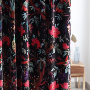 Puede incluir: Cortina de terciopelo negro con un vibrante estampado floral y de pájaros. El diseño presenta flores rojas, hojas turquesas y pájaros coloridos sobre un fondo oscuro. La cortina está hecha de una tela suave y fluida, añadiendo elegancia.