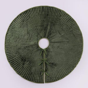 Puede incluir: Una falda de &aacute;rbol redonda, verde oliva, con textura acanalada. La falda tiene una abertura circular en el centro y est&aacute; dividida por delante, asegurada con lazos verdes. El borde est&aacute; rematado con un borde verde m&aacute;s oscuro.
