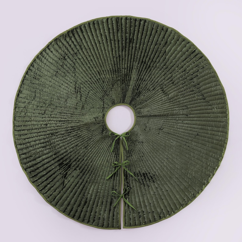 Puede incluir: Una falda de &aacute;rbol redonda, verde oliva, con textura acanalada. La falda tiene una abertura circular en el centro y est&aacute; dividida por delante, asegurada con lazos verdes. El borde est&aacute; rematado con un borde verde m&aacute;s oscuro.