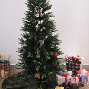 Puede incluir: Un &aacute;rbol de Navidad artificial decorado con una estrella dorada, adornos y campanas plateadas. Una falda de &aacute;rbol verde rodea la base. Regalos envueltos en papel de colores est&aacute;n colocados alrededor del &aacute;rbol, creando un ambiente festivo.